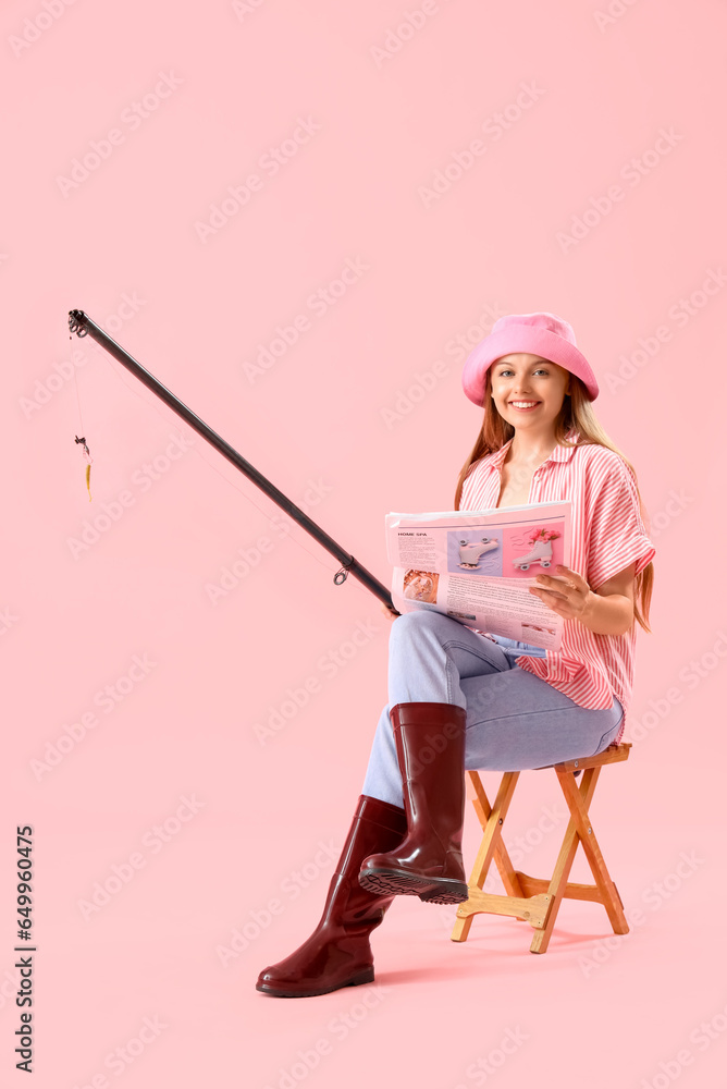 Happy young woman with fishing rod and newspaper on pink background