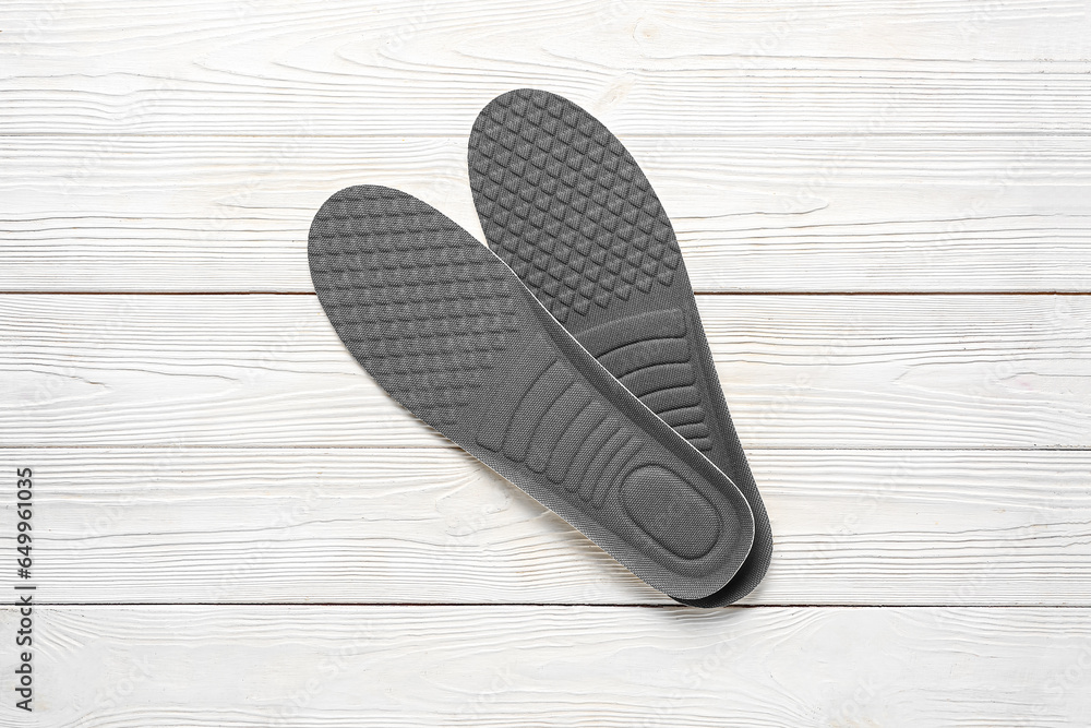 Pair of orthopedic insoles on light wooden background