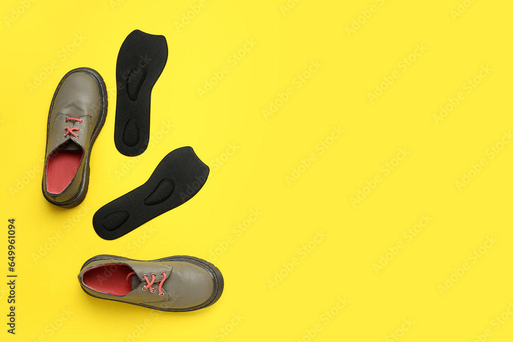 Pair of stylish shoes and orthopedic insoles on yellow background