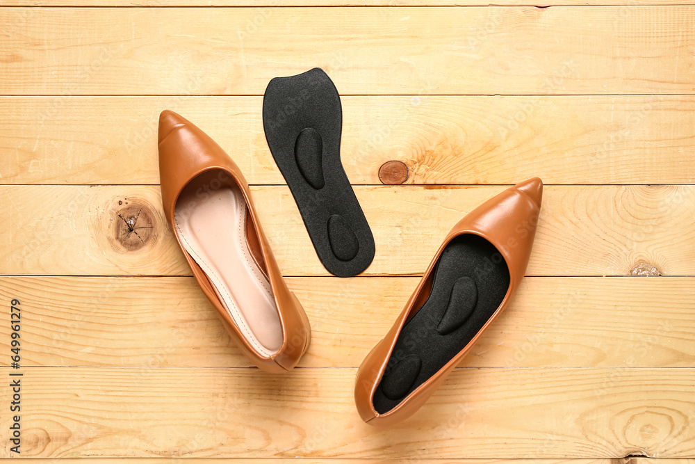 Pair of stylish female shoes and orthopedic insoles on wooden background