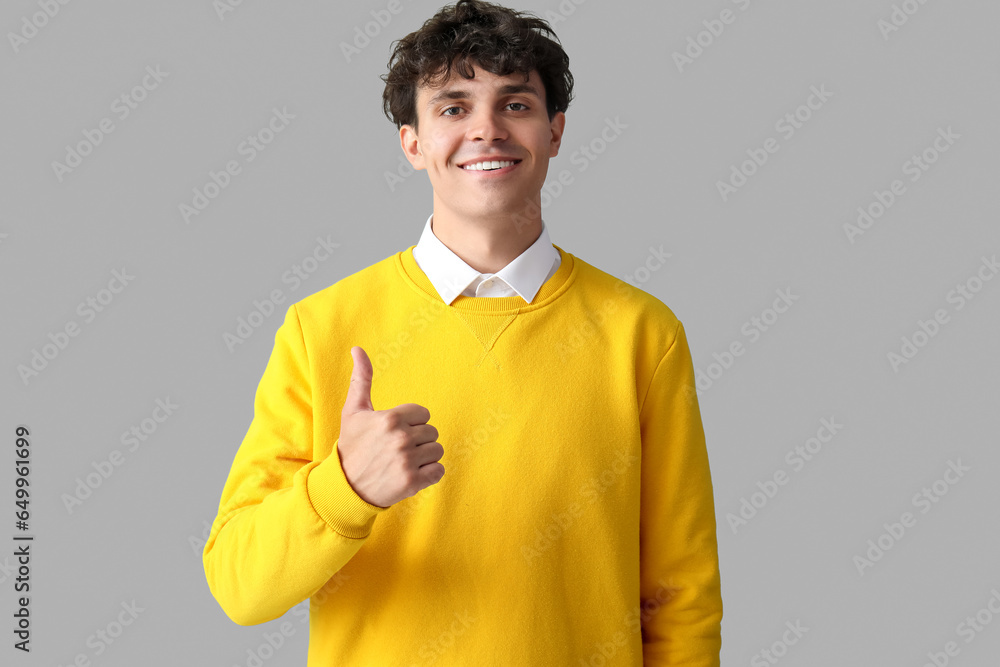 Portrait of handsome young man showing thumb up on grey background