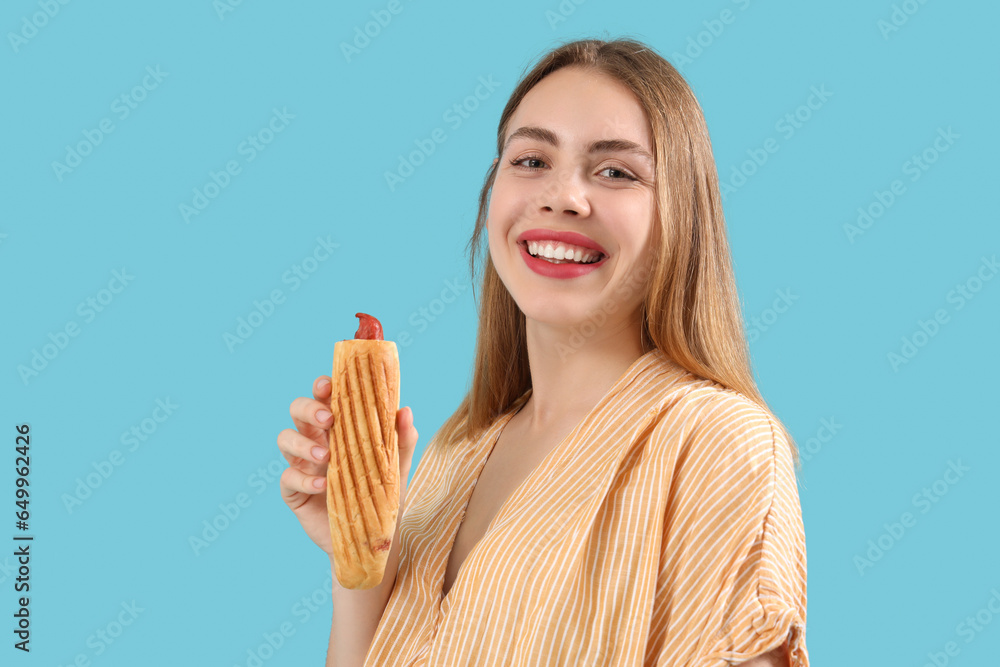 Pretty young woman with tasty french hot dog on blue background