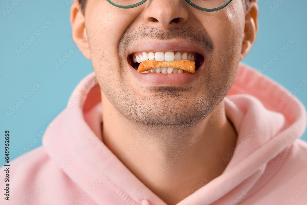 Young man eating french fries on blue background, closeup