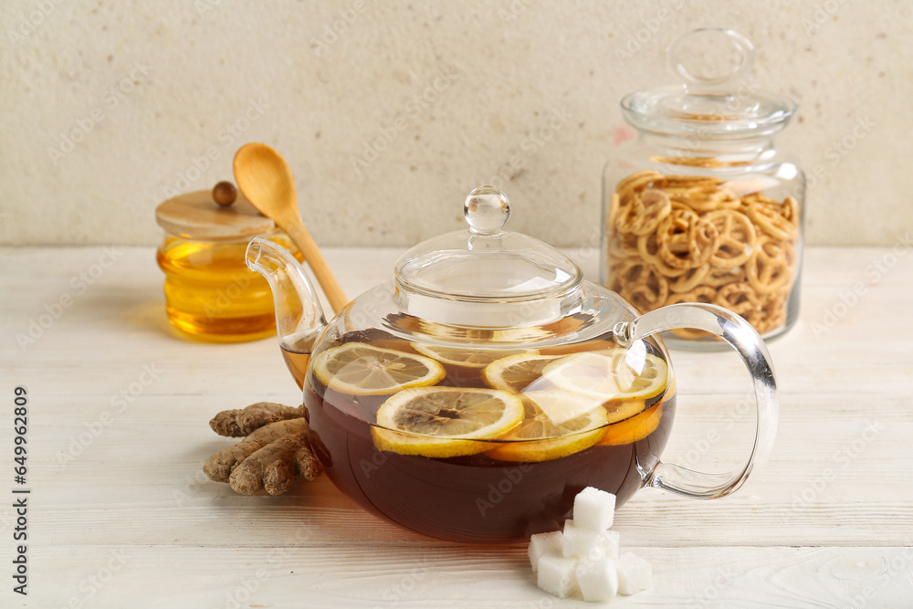 Glass teapot with hot tea, honey and pretzels on light wooden table