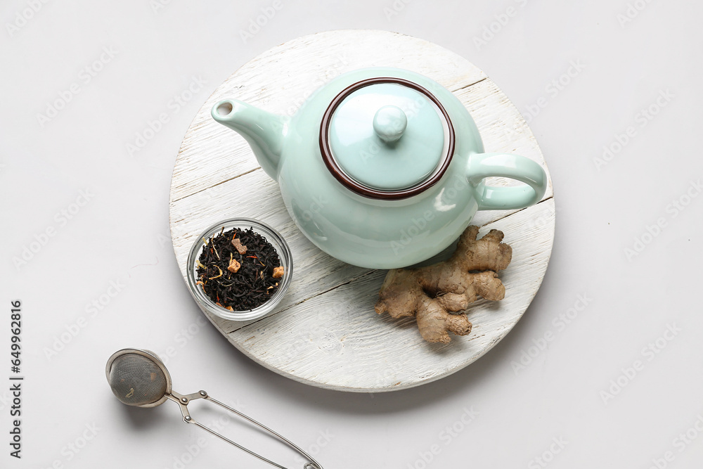 Wooden board with teapot, dried tea and ginger root on light background