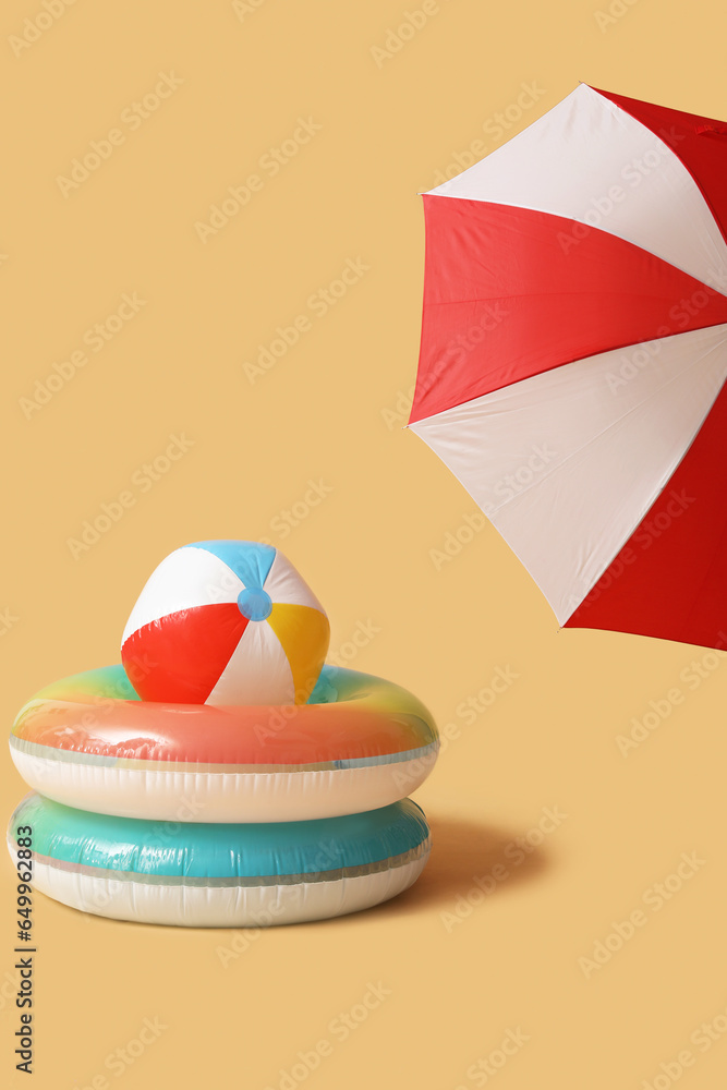 Swim rings with beach ball and umbrella on beige background