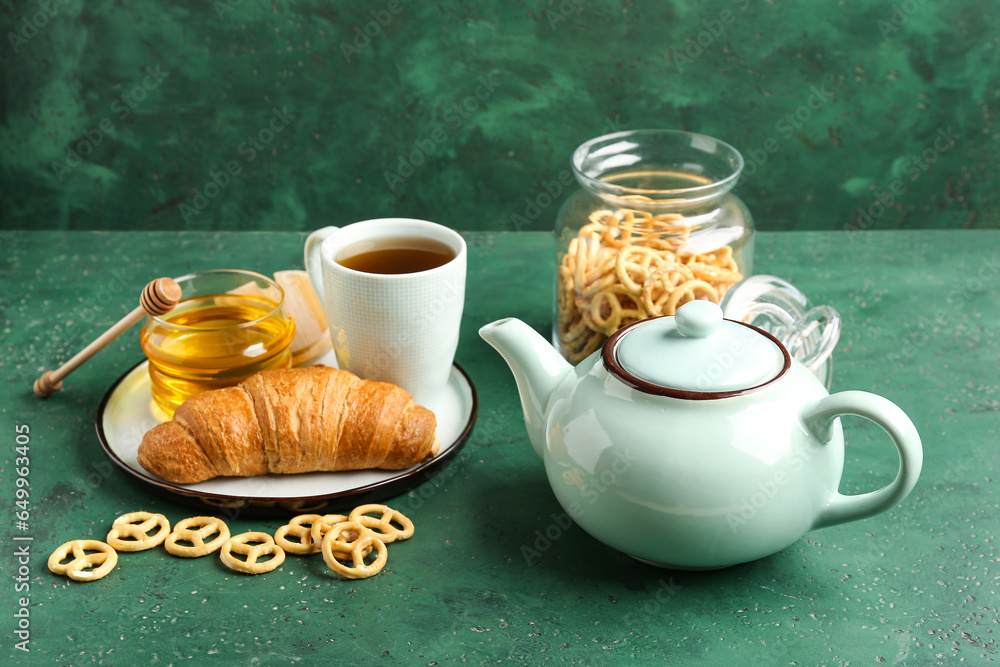 Composition with cup of tea, teapot, snacks and croissant on green table