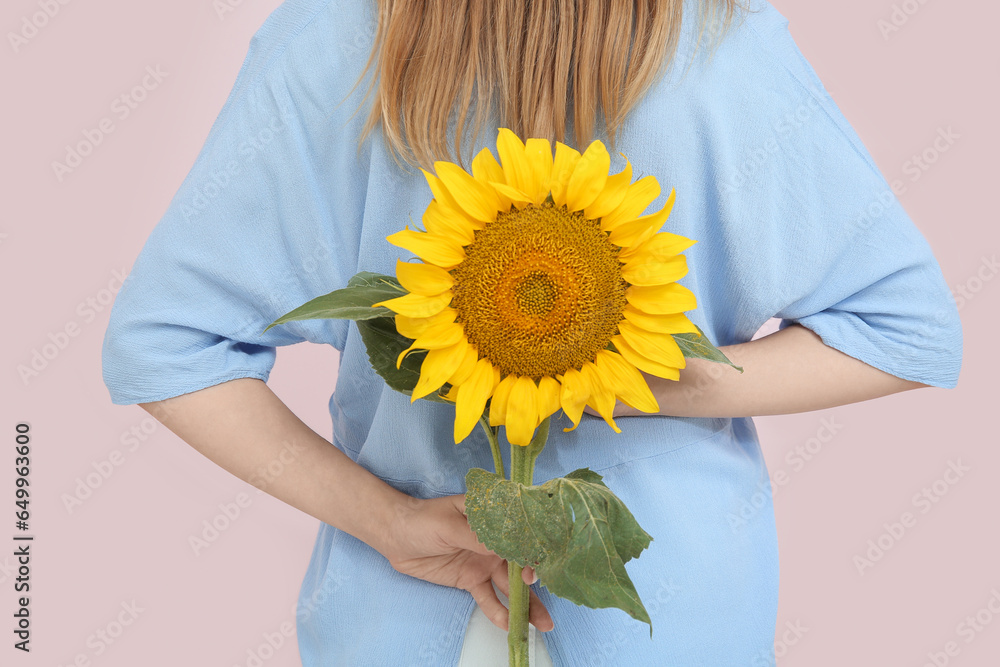 Woman with beautiful sunflower on beige background, back view