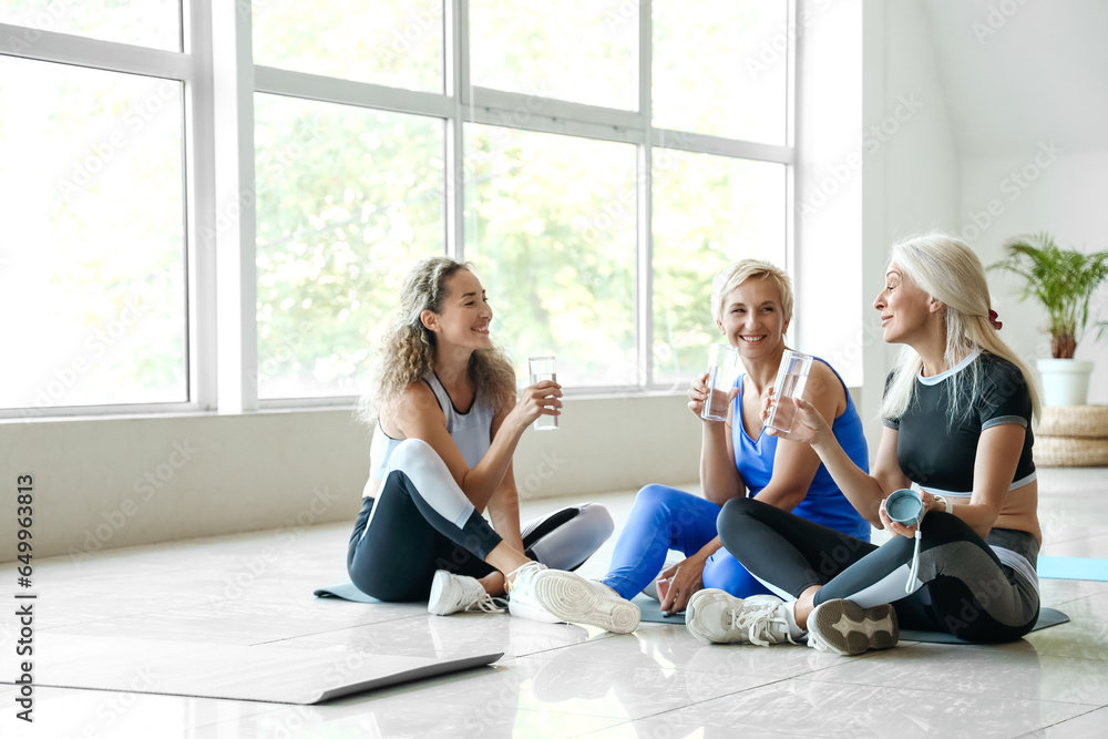 Sporty mature women drinking water after practicing yoga in gym