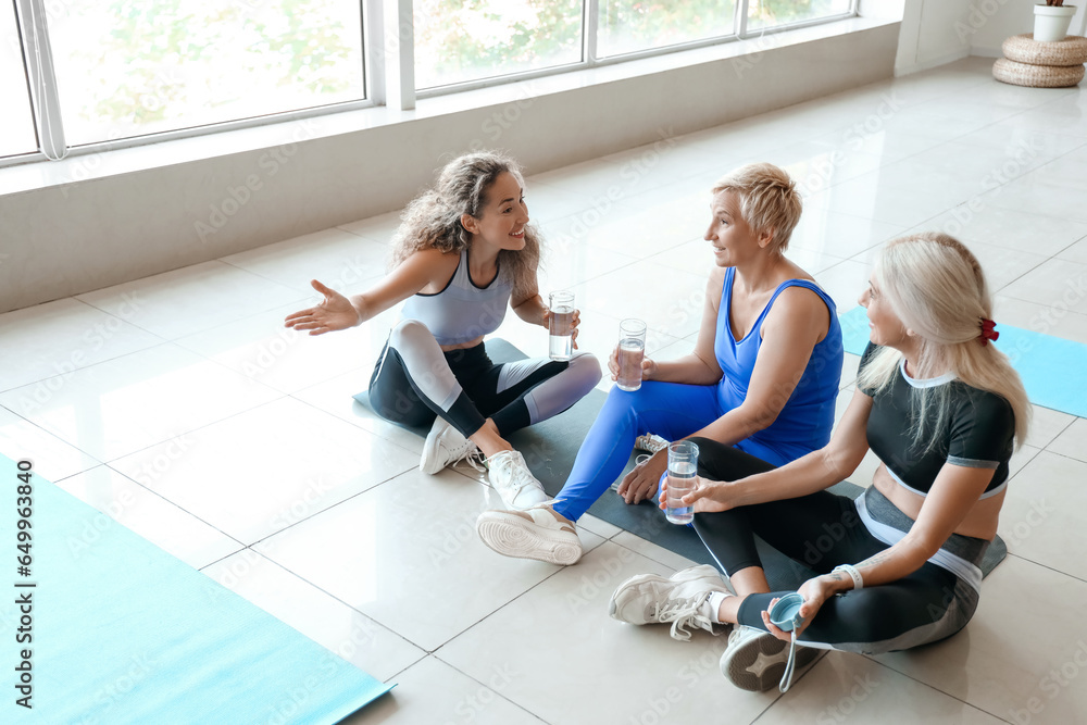 Sporty mature women drinking water after practicing yoga in gym