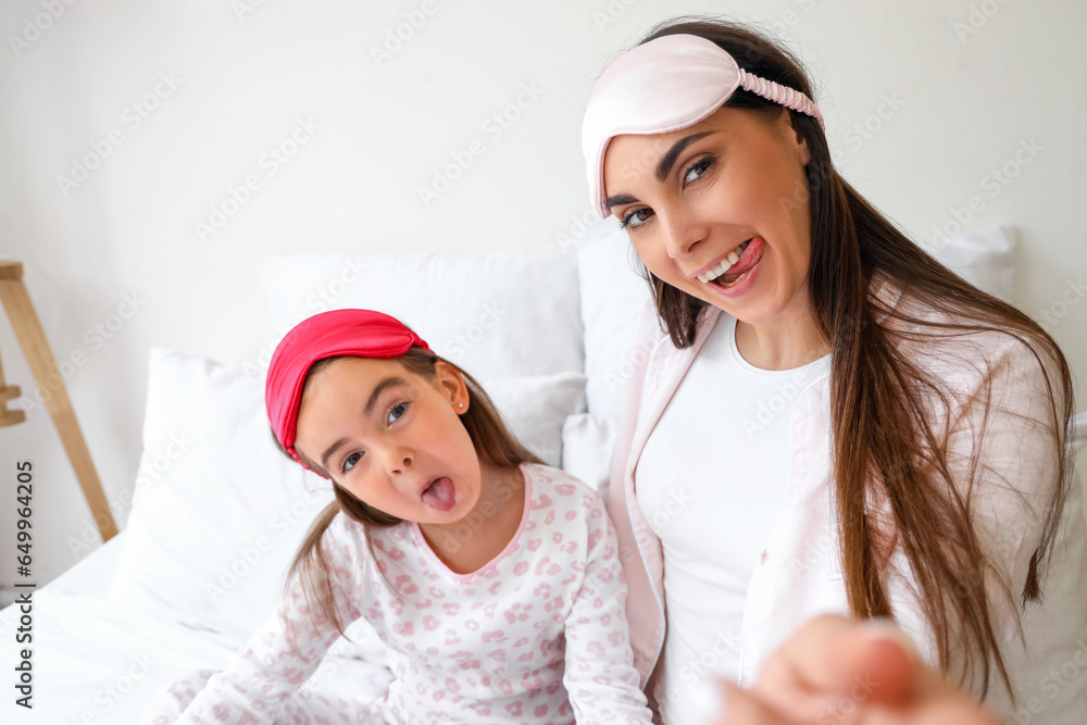 Happy mother and her little daughter with sleeping masks in bedroom