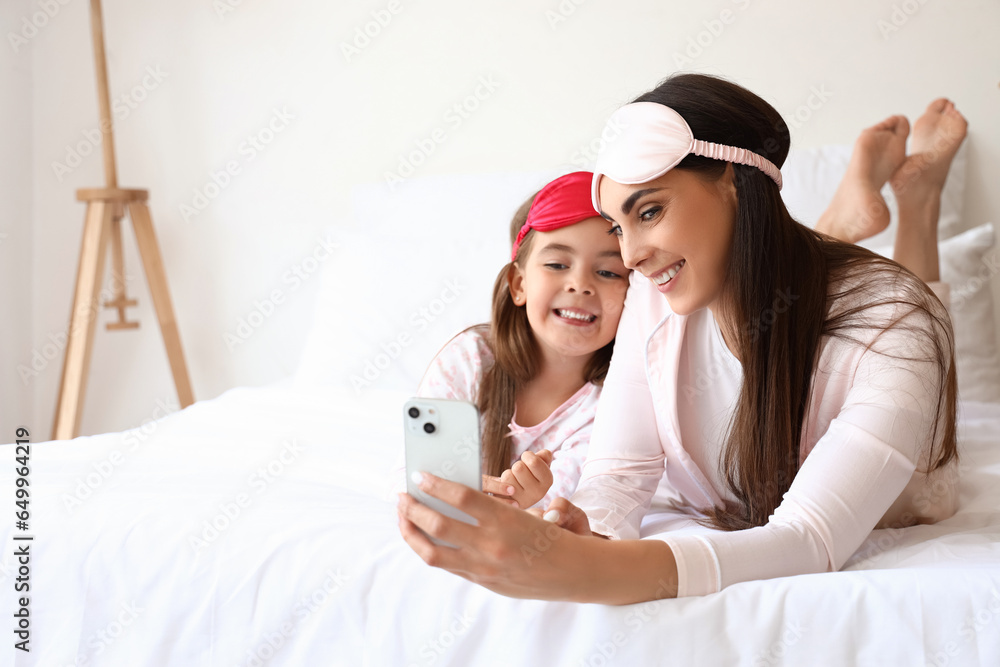 Happy mother and her little daughter with sleeping masks taking selfie in bedroom