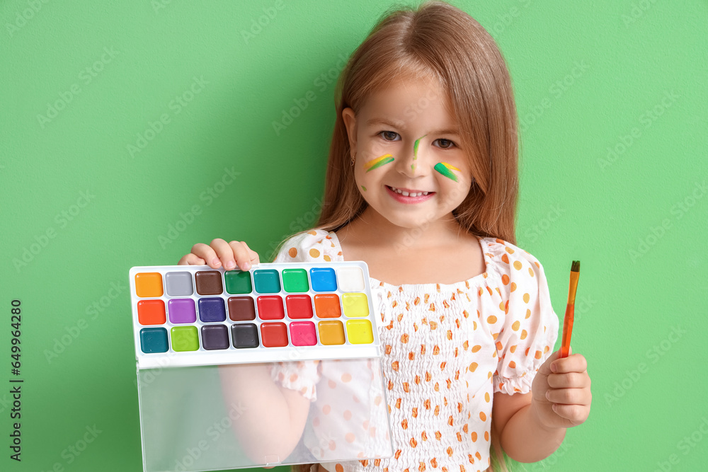 Cute little girl with paints on green background