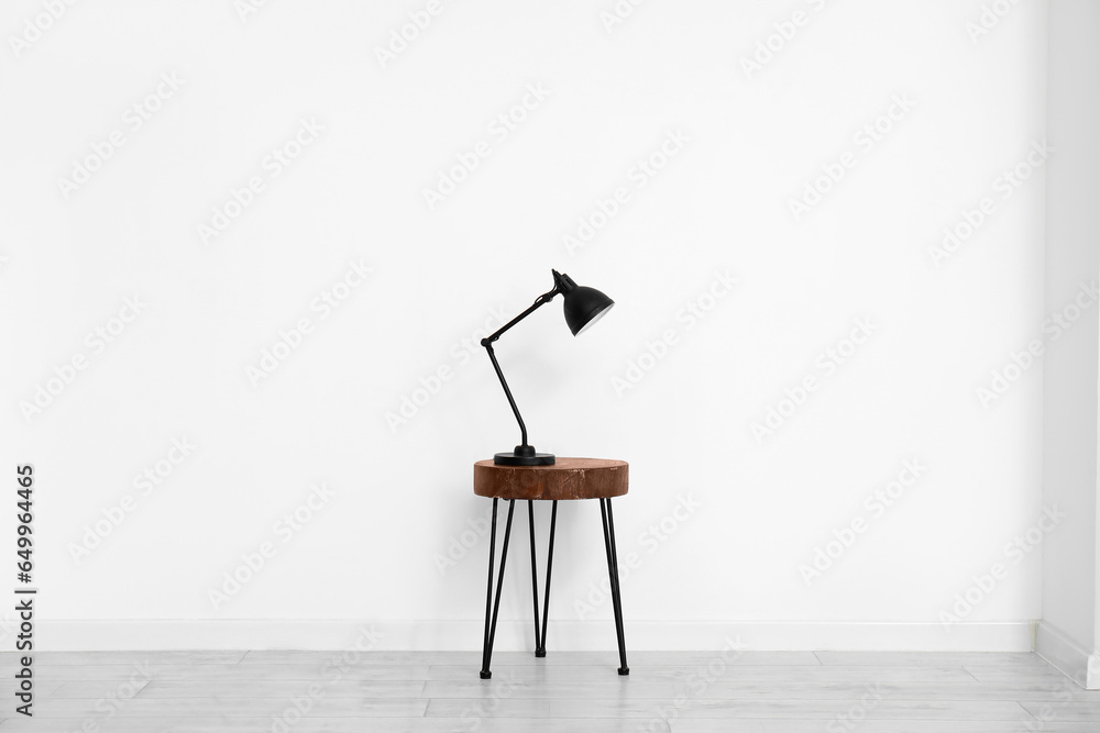 Desk lamp on small wooden table near white wall