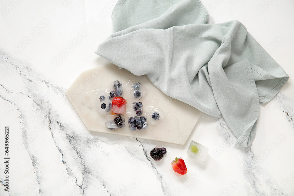 Board with frozen berries in ice cubes on white background