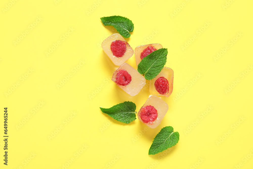 Frozen raspberries in ice cubes and mint on yellow background