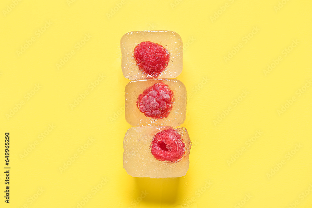 Frozen raspberries in ice cubes on yellow background