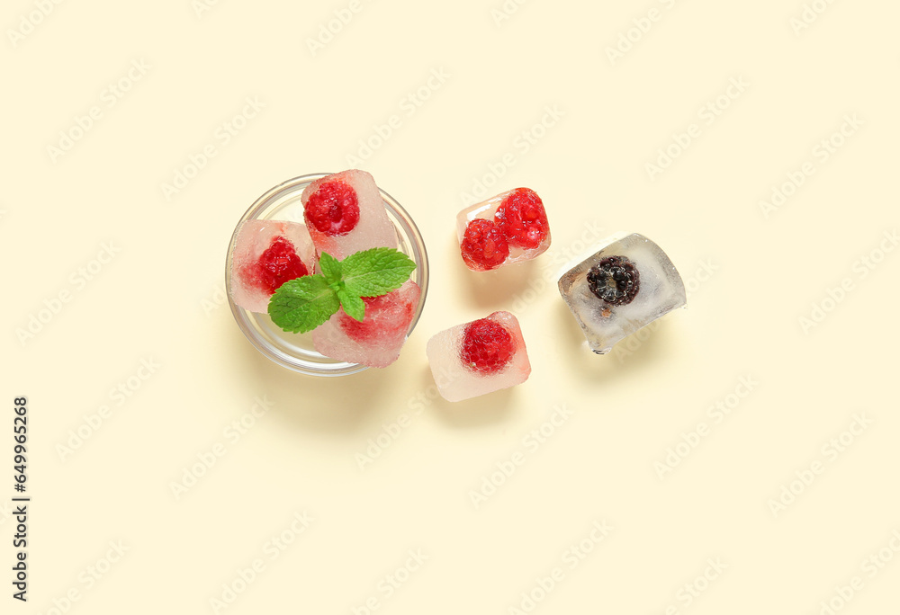 Glass bowl with frozen berries in ice cubes and mint on yellow background