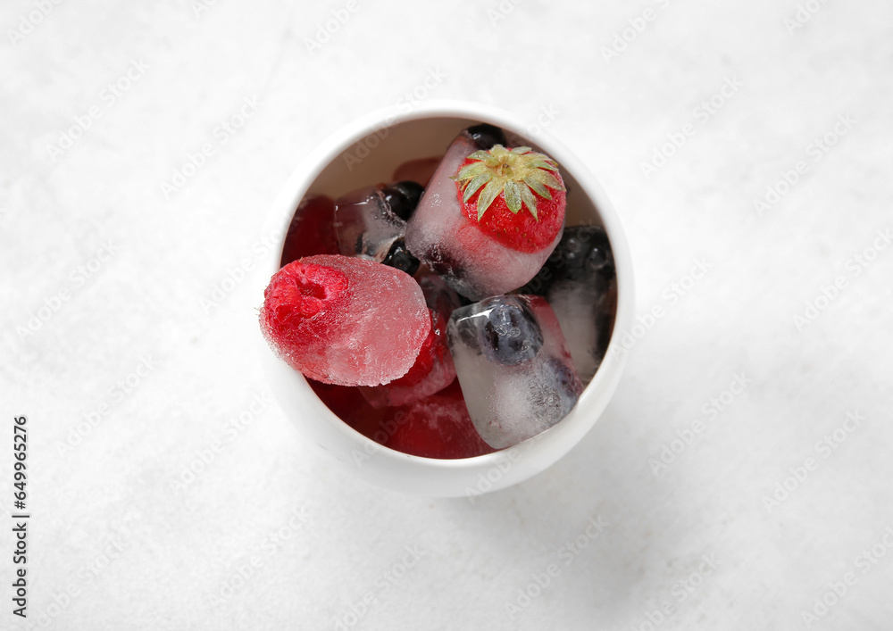 Bowl with frozen berries in ice cubes on white background