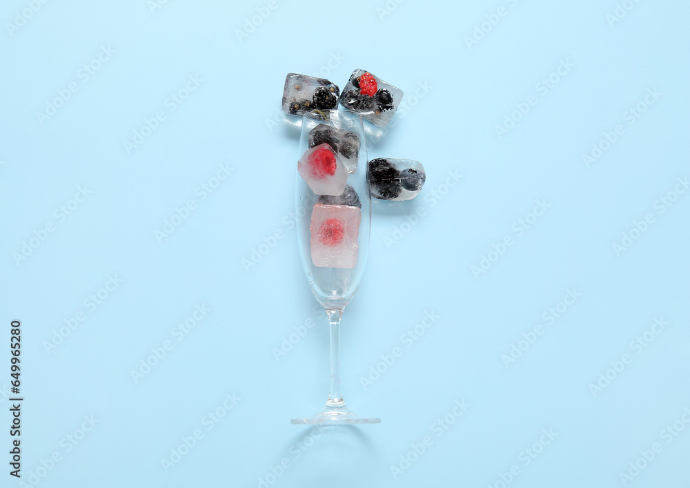 Glass with frozen berries in ice cubes on blue background