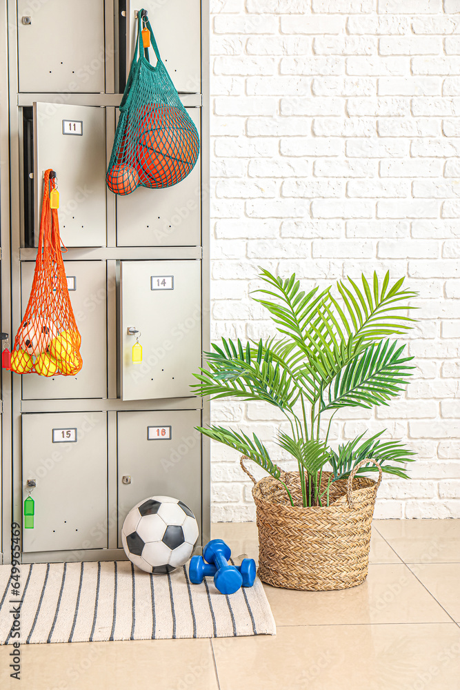 Modern locker with sports equipment near white brick wall