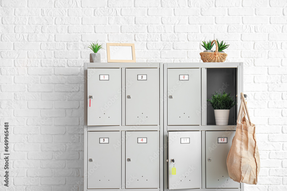 Modern locker with plants and bag near white brick wall