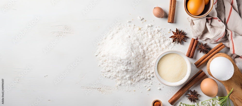 Flat lay baking background with flour eggs sugar spices and whisk on a white tabletop