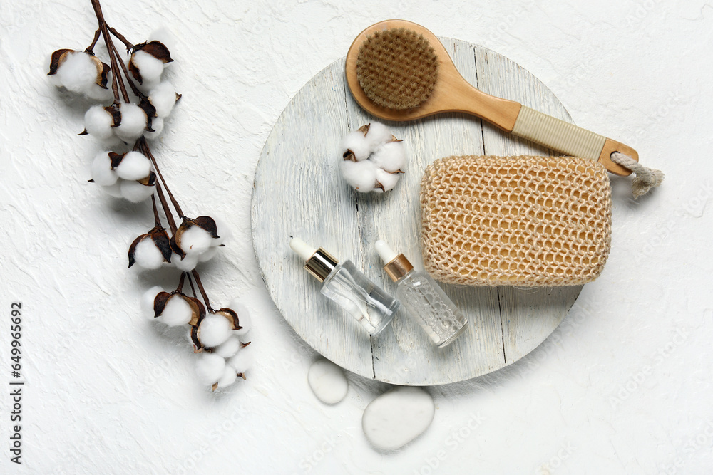 Composition with bottles of essential oil, bath supplies and cotton branch on light background