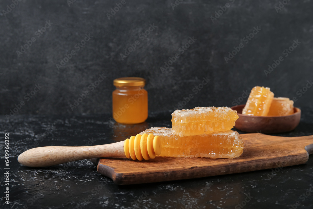 Wooden board with sweet honeycombs and dipper on dark background