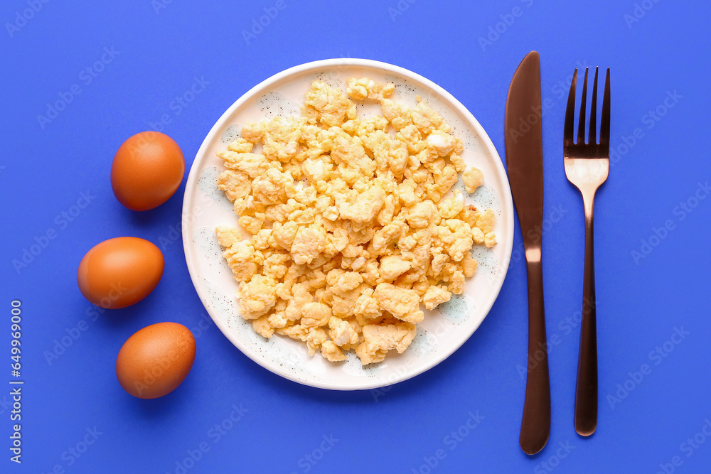 Plate of tasty scrambled eggs on blue background