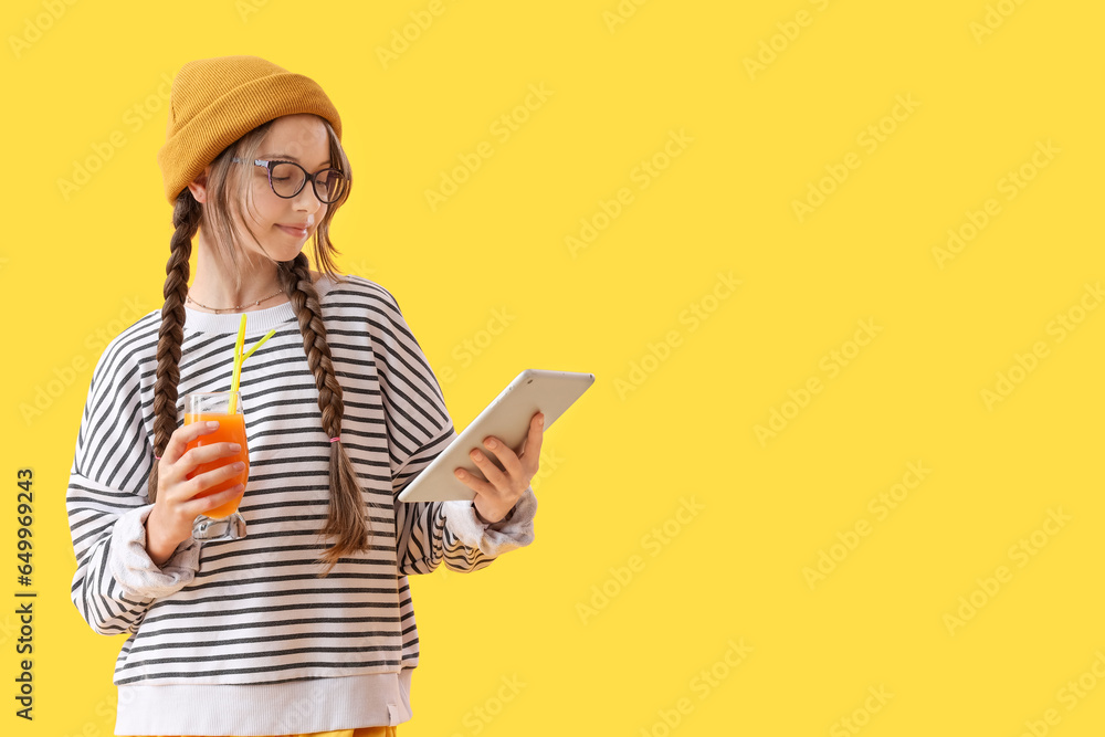 Little girl with glass of juice and tablet computer on yellow background