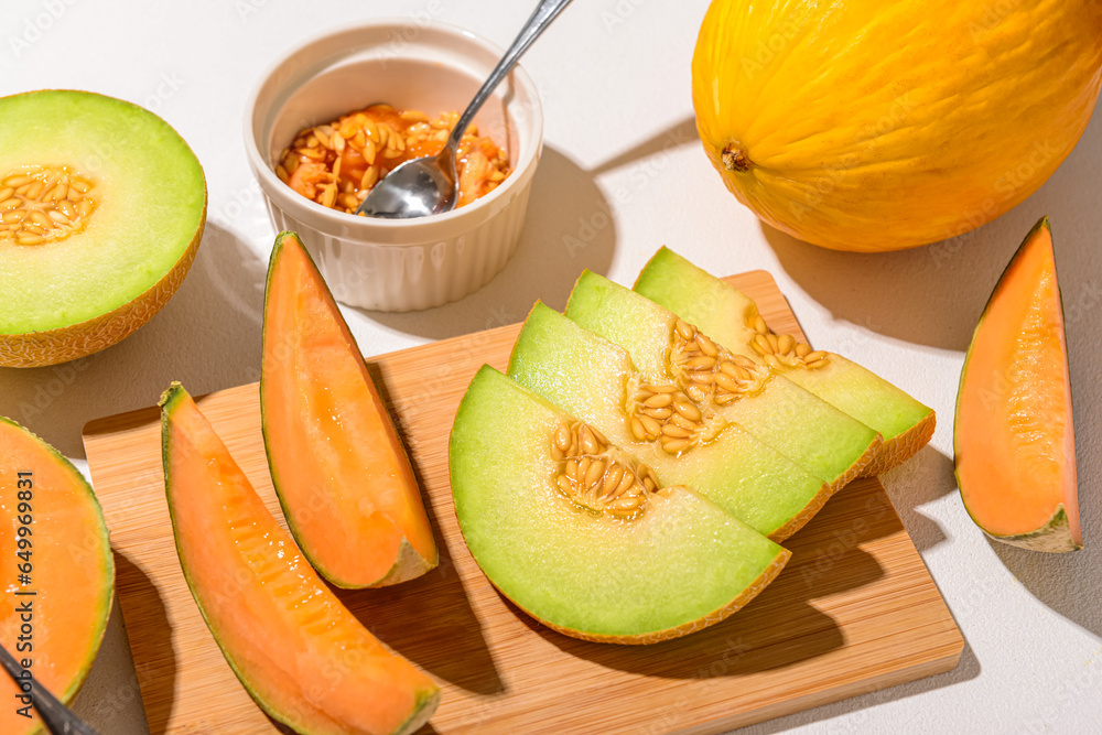 Wooden board with ripe cut melons on white background