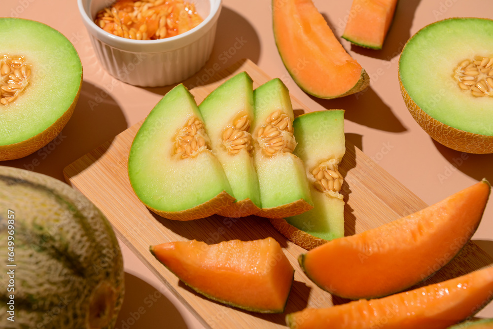 Wooden board with ripe cut melons on orange background