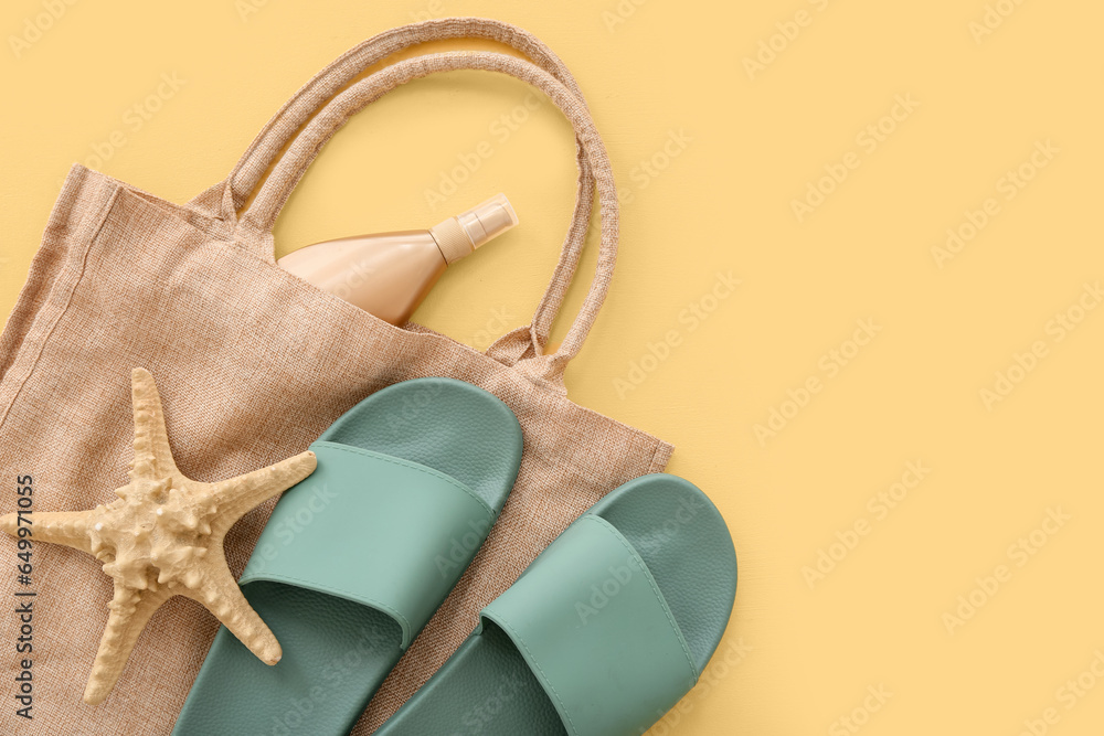 Pair of green flip flops with bag and sunscreen cream on yellow background