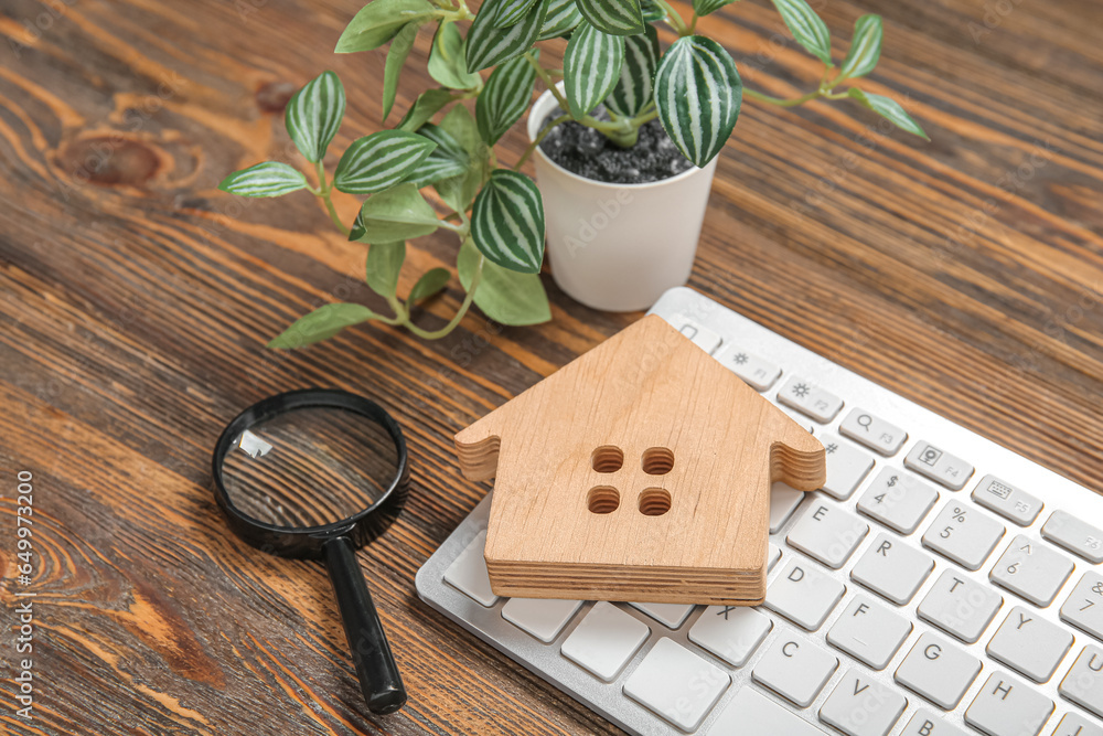 House figure with keyboard and magnifier on brown wooden background. Concept of buying real estate