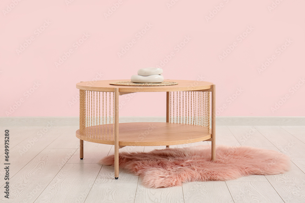 Wooden coffee table and fur rug near pink wall