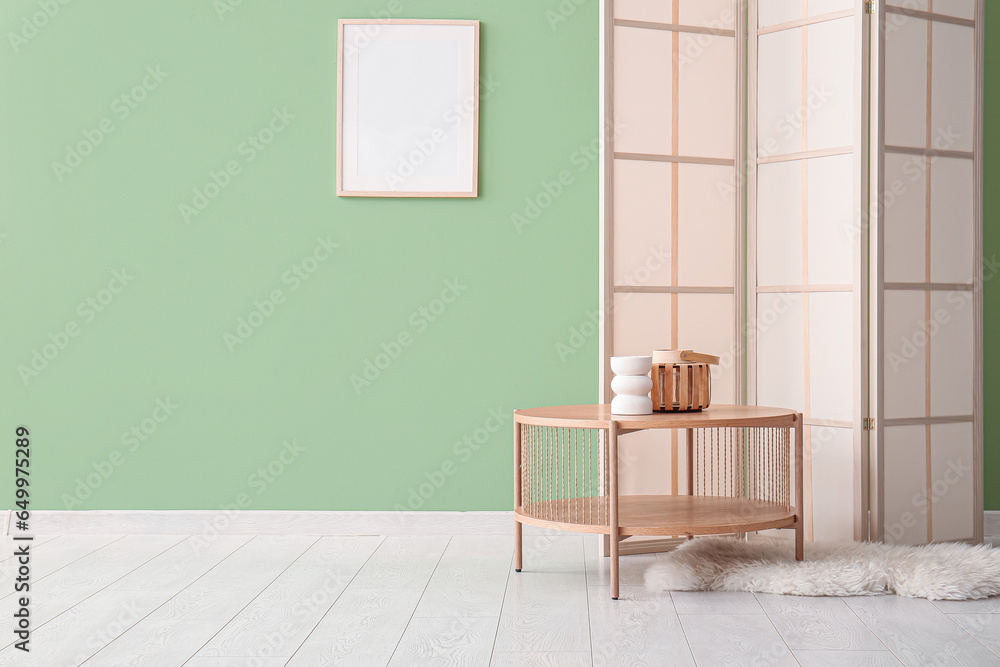 Wooden coffee table with decor and folding screen near green wall