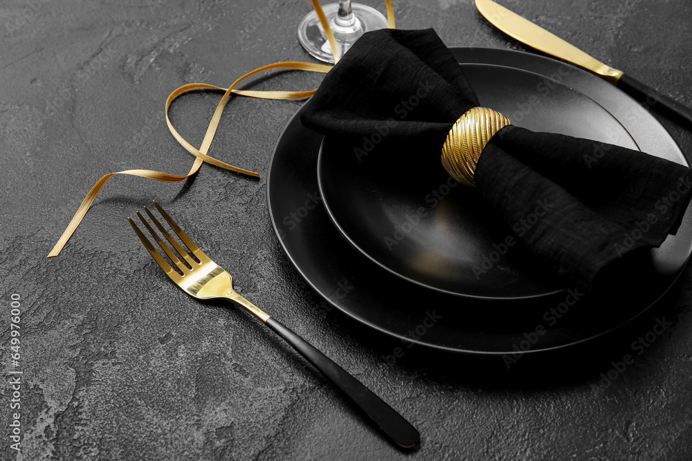 Elegant table setting with golden cutlery and folded napkin on black background, closeup