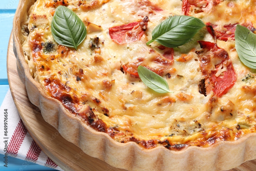 Tasty quiche with tomatoes, basil and cheese on light blue table, closeup