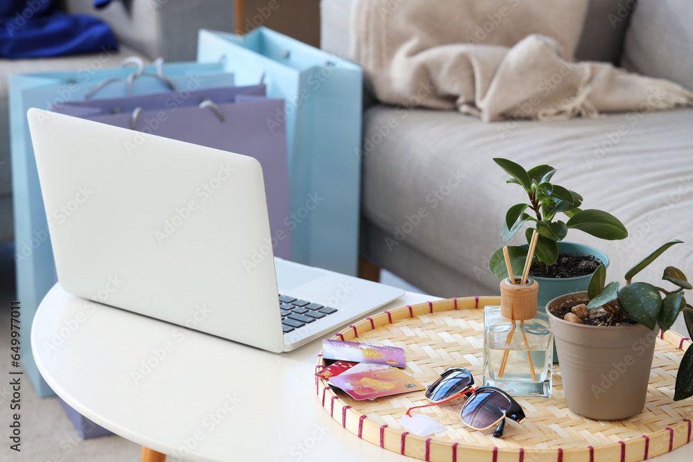 Laptop with credit cards and sunglasses on table in living room. Online shopping