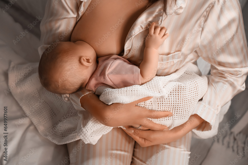 Young woman breastfeeding her baby in bedroom at night, closeup