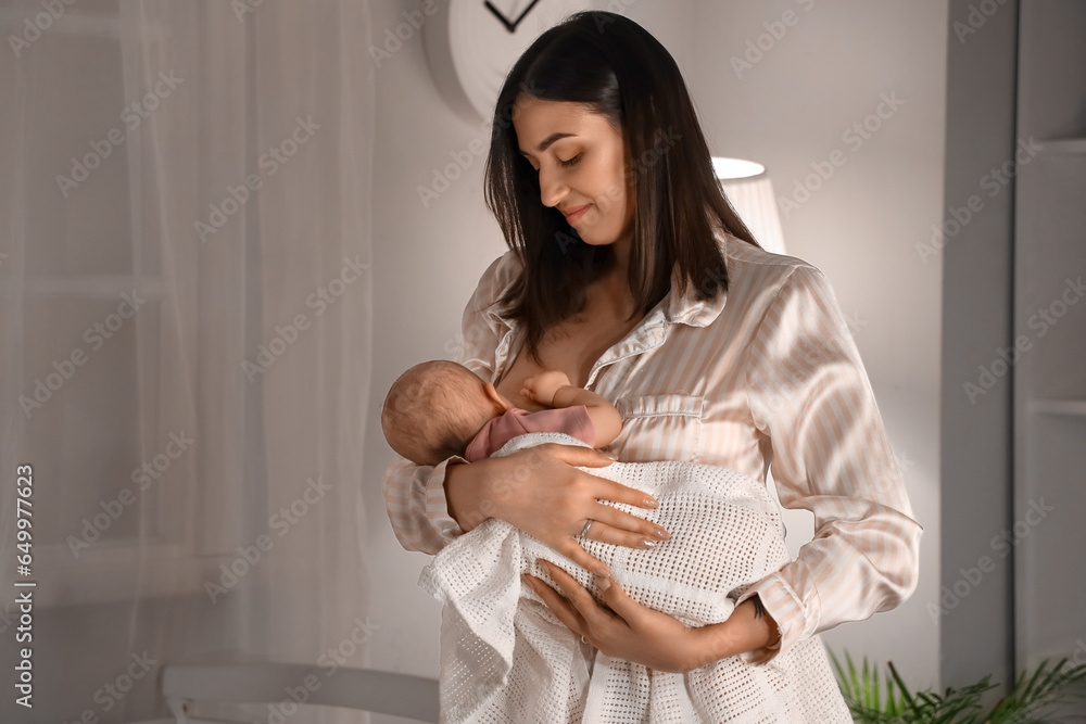 Young woman breastfeeding her baby in bedroom at night