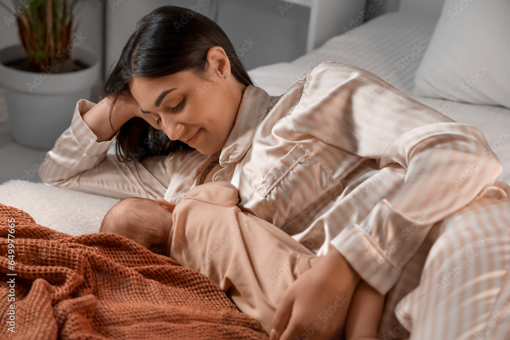 Young woman breastfeeding her baby in bedroom at night