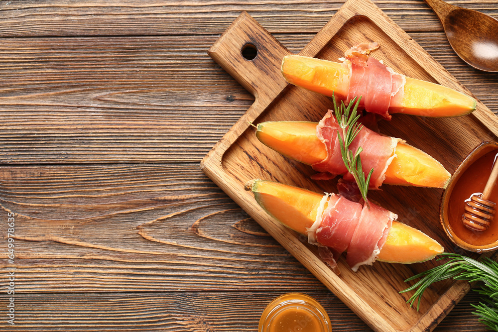 Cutting board with tasty melon, prosciutto and honey on wooden background