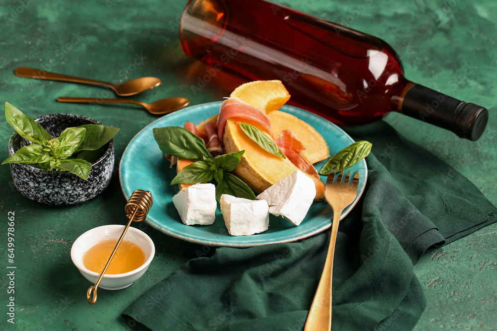 Composition with tasty melon, prosciutto, cheese and bottle of wine on color background