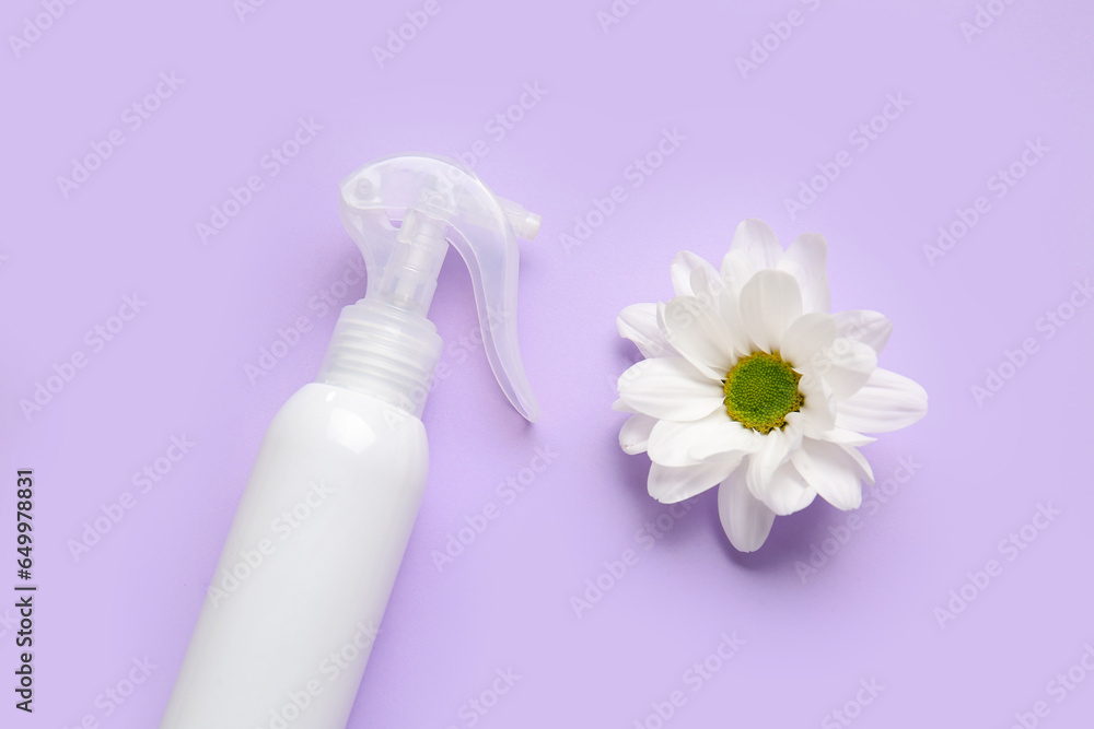 Bottle of cosmetic product and chamomile flower on lilac background, closeup