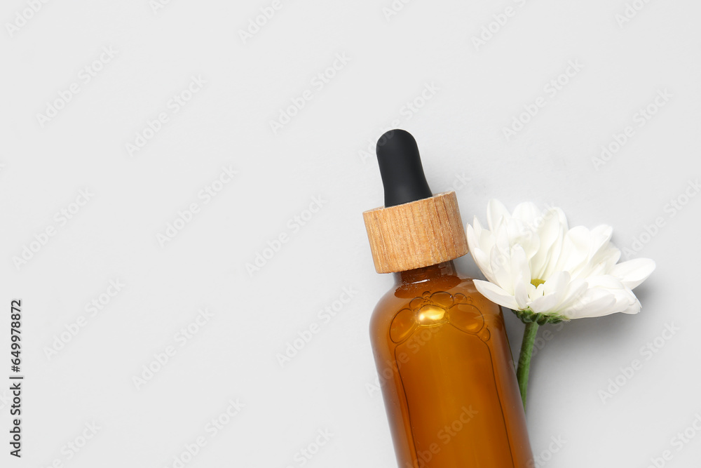 Bottle of essential oil with chamomile flower on light background