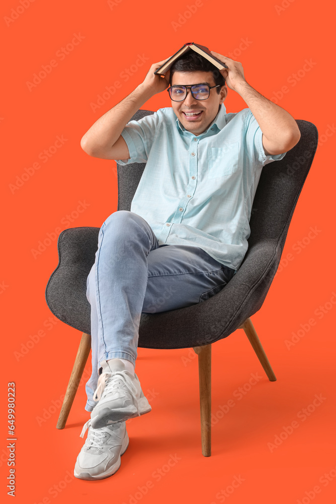 Young man reading book in armchair on red background