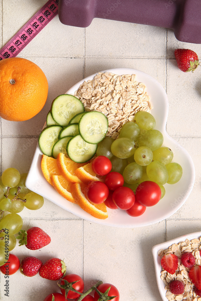 Plate with fresh healthy products, measuring tape and dumbbell on light tile background. Diet concept