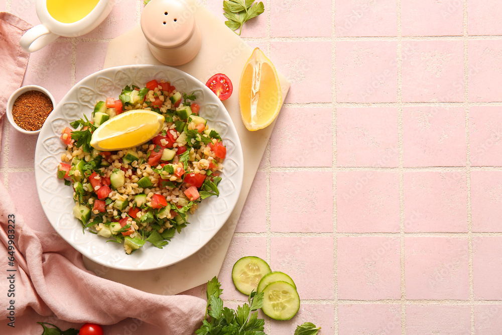 Plate with delicious tabbouleh salad and lemon on pink tile background